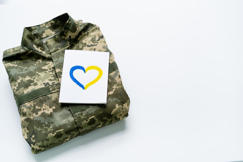 Karte von oben mit blauem und gelbem Herzzeichen auf Militäruniform auf weißem Hintergrund - Foto, Bild