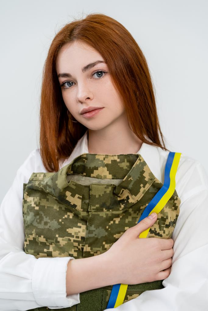 Portrait of young woman holding military uniform with blue and yellow ribbon isolated on white  - Photo, Image