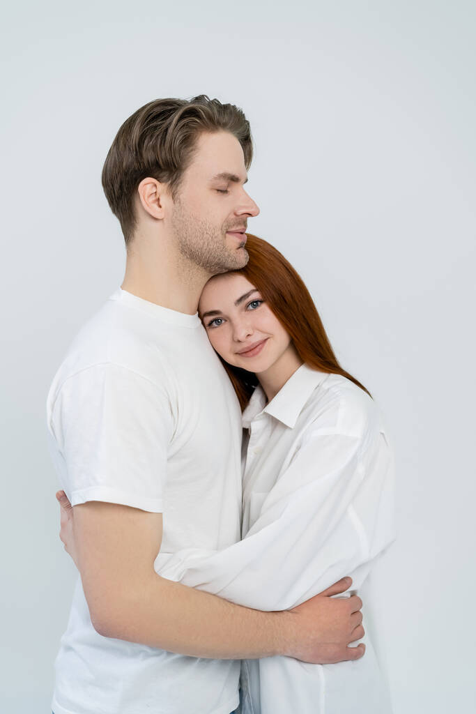 Θετική κοκκινομάλλα γυναίκα αγκαλιάζει φίλο απομονωμένο σε λευκό  - Φωτογραφία, εικόνα