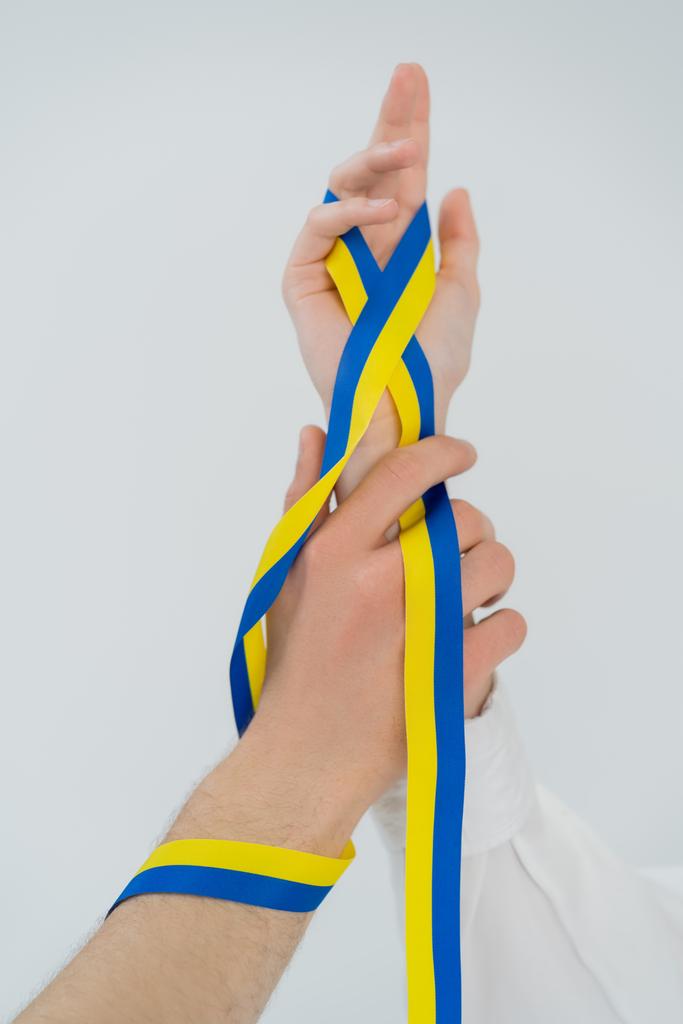 Gekropte weergave van blauw en geel lint op handen van jong paar geïsoleerd op wit  - Foto, afbeelding
