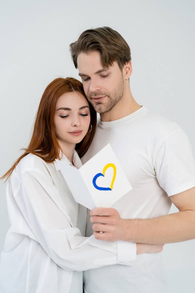 Мужчина держит карточку с голубым и желтым знаком сердца рядом с девушкой изолированы на белом  - Фото, изображение