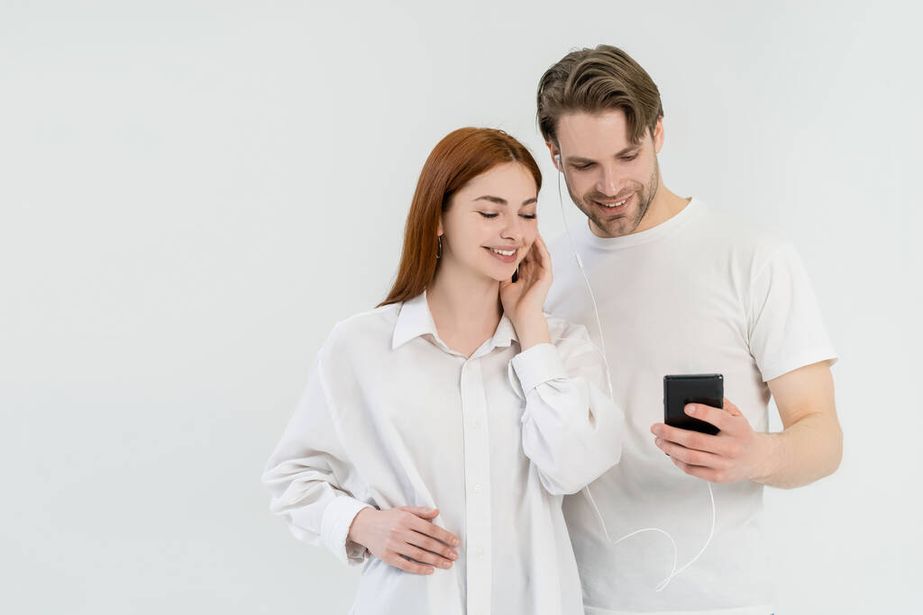 Veselý pár pomocí mobilu a sluchátek izolovaných na bílém  - Fotografie, Obrázek