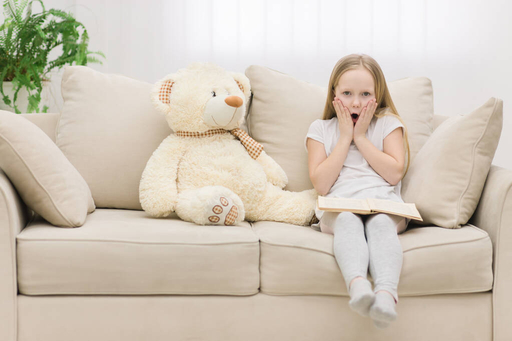 Cropped photo of surprised little girl touching her face with hands near teddy bear. - Photo, Image