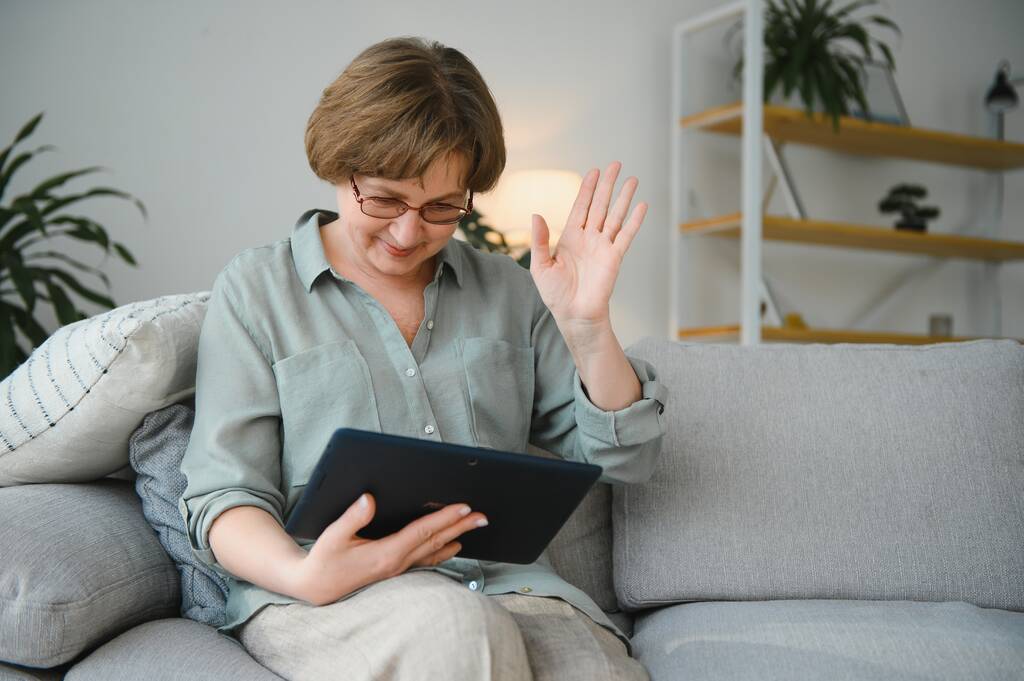Wypoczynek na emeryturze. Uśmiechnięta starsza kobieta odpoczywająca z tabletem cyfrowym na kanapie w domu, przeglądająca Internet lub oglądająca filmy. - Zdjęcie, obraz