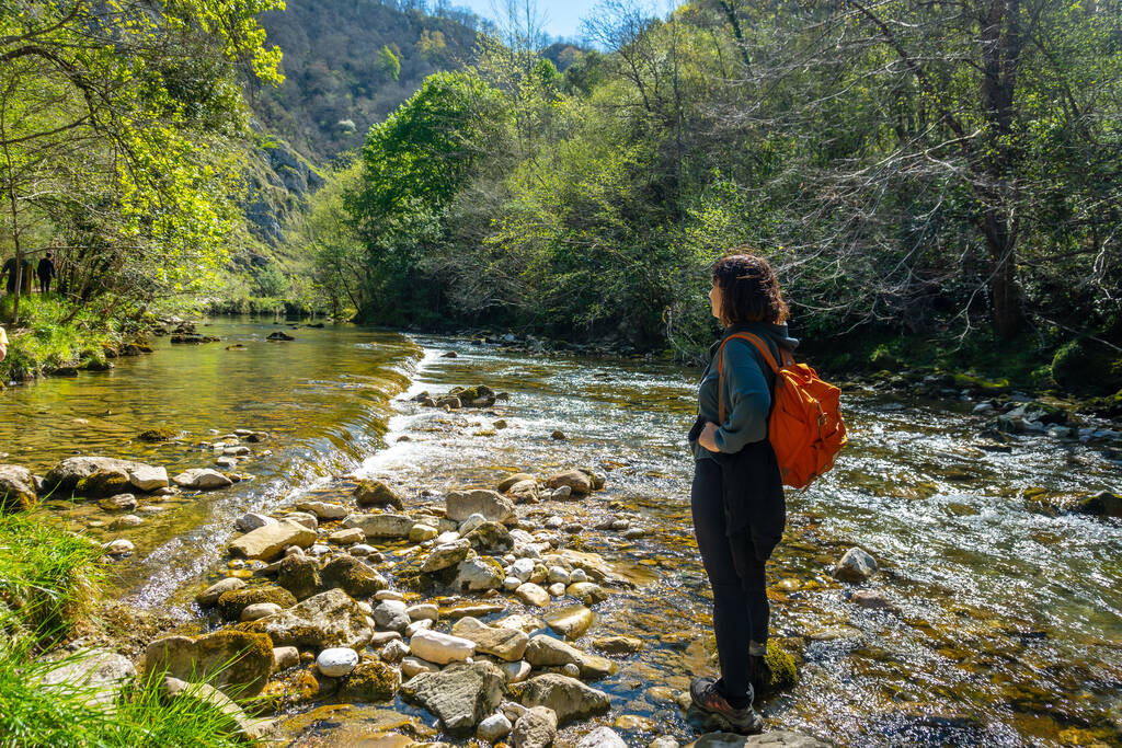 A young woman with a backpack in the Sella river on the path between the Tornin to the Olla de San Vicente, near Cangas de Onis. Asturias. Spain - Photo, image