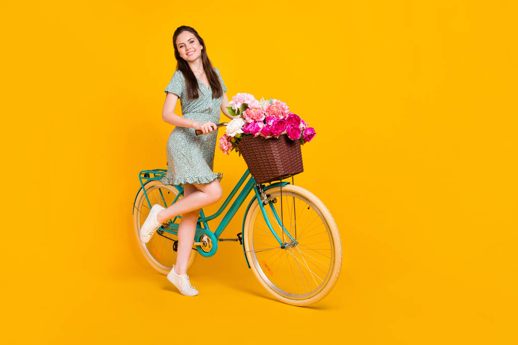 Фото блискучої солодкої молодої жінки в сукні з принтом їзда на велосипеді рожевий пучок ізольований жовтий кольоровий фон
 - Фото, зображення