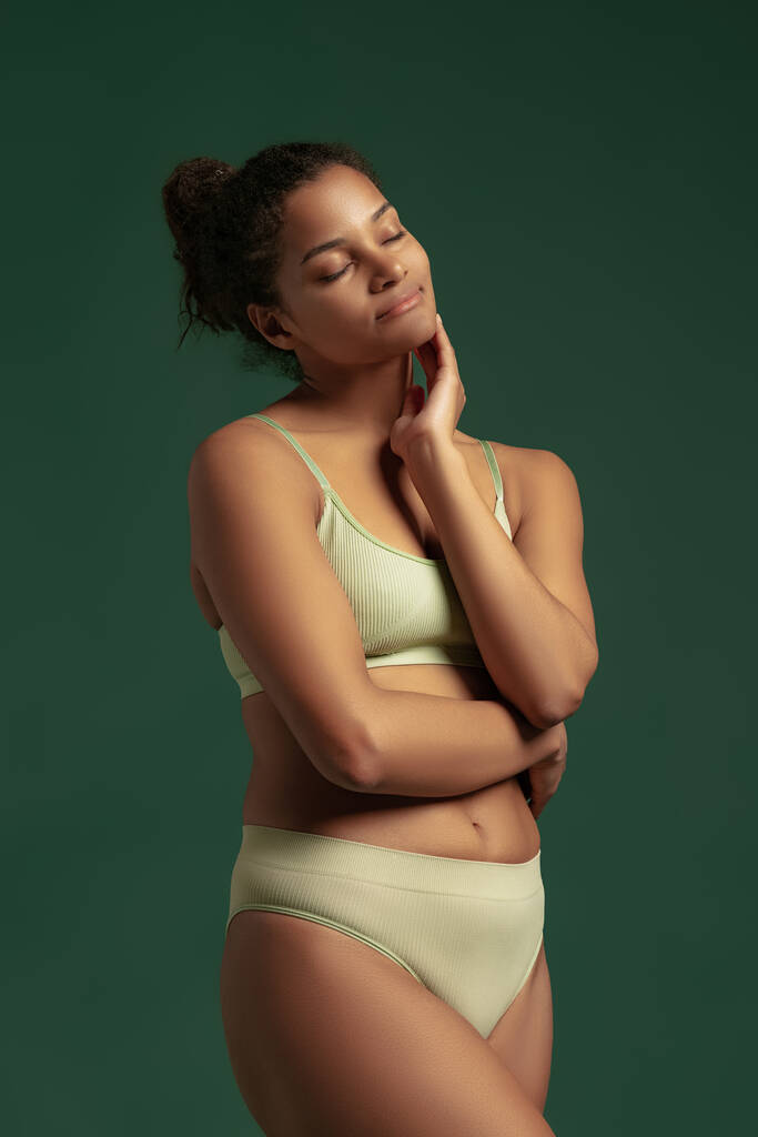 Portrait of young tender woman posing in comfortable cotton underwear isolated over green studio background. Natural beauty - Photo, Image