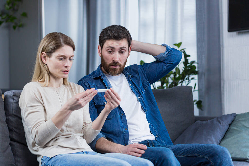 Trauriger Mann und Frau auf der Couch, enttäuscht über negativen Schwangerschaftstest - Foto, Bild