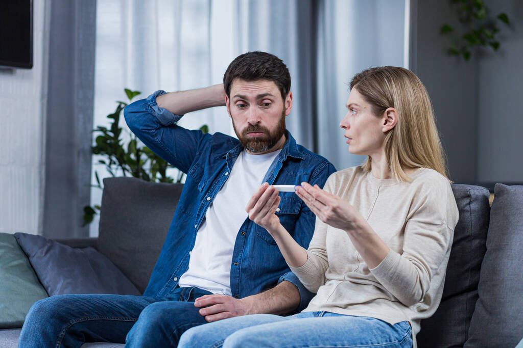 Smutný muž a žena sedí na gauči, zklamáni negativním těhotenským testem - Fotografie, Obrázek