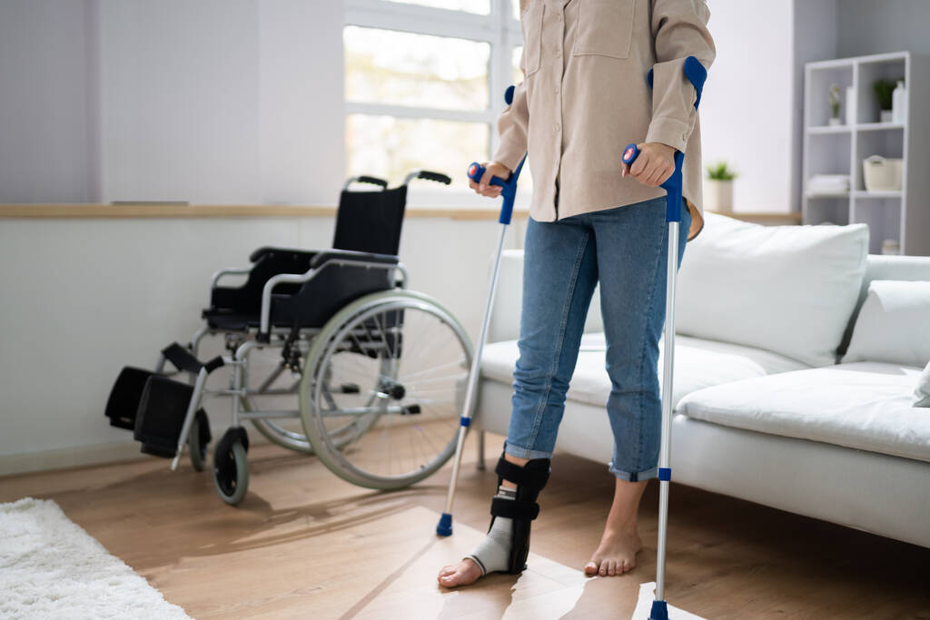Pijn been met behulp van krukken in de buurt van een rolstoel thuis - Foto, afbeelding