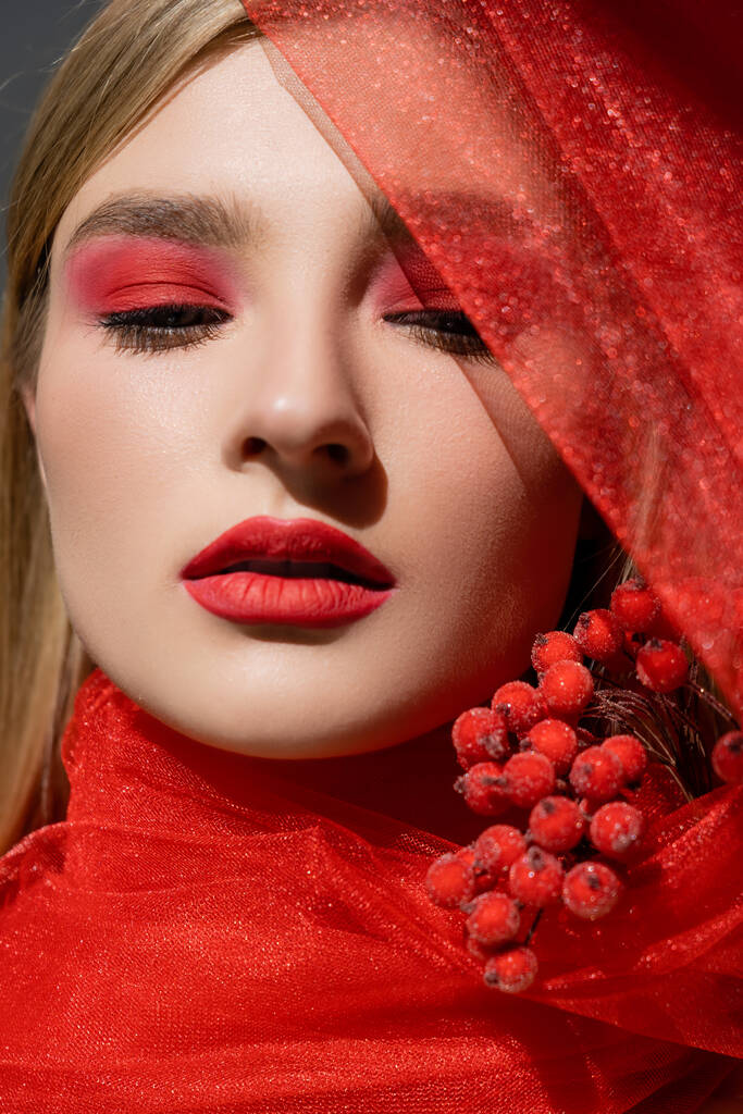 Retrato de modelo bonito con rostro rojo posando cerca de tela y bayas aisladas en gris  - Foto, imagen