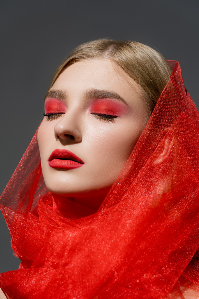 Young model with red eye shadow and cloth closing eyes isolated on grey  - Photo, Image