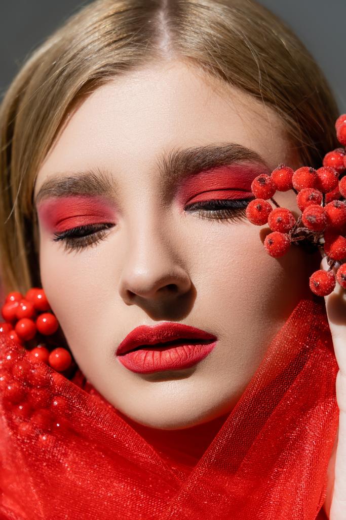 Πορτρέτο του όμορφου μοντέλου με κόκκινη όψη που ποζάρει κοντά σε ύφασμα και μούρα που απομονώνονται σε γκρι  - Φωτογραφία, εικόνα