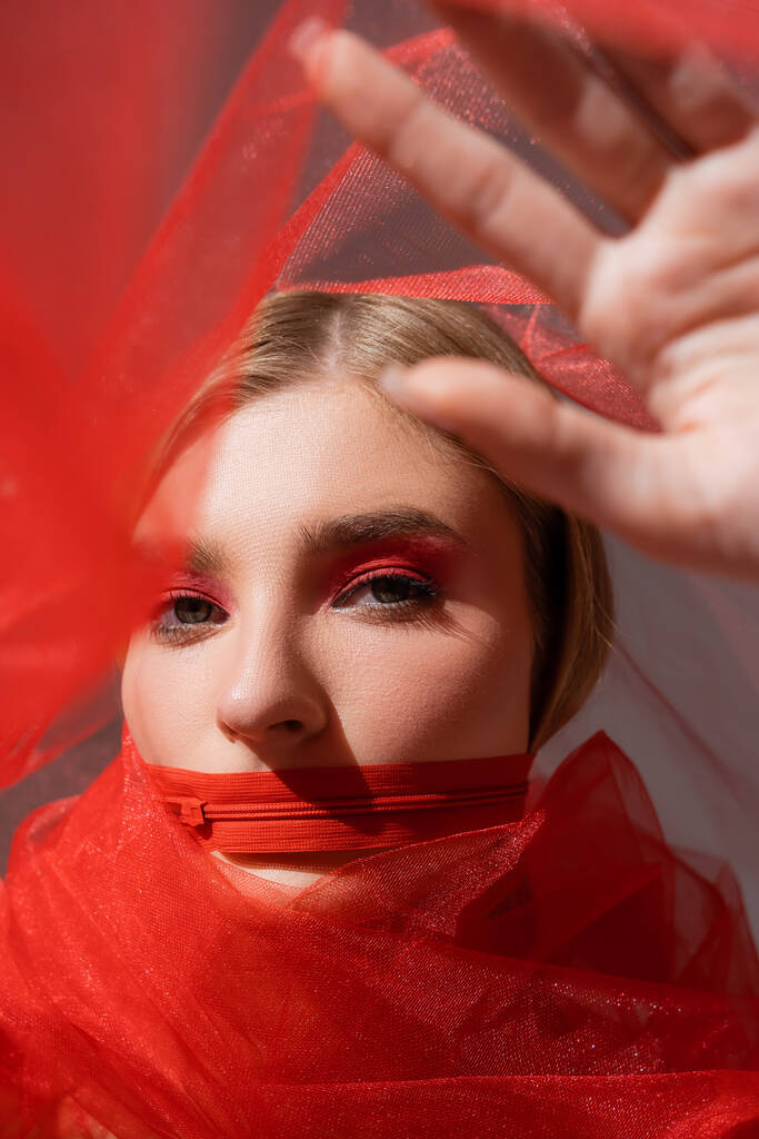 Szép hajú nő piros cipzárral a száján gazdaság ruha szürke háttér  - Fotó, kép