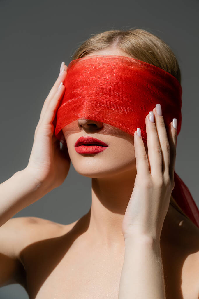 Woman with naked shoulders and red lips touching cloth on face isolated on grey  - Photo, Image