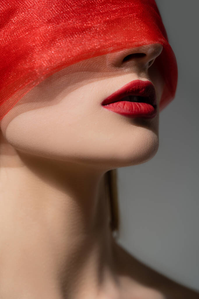 Γυναίκα με κόκκινα χείλη και ύφασμα στο πρόσωπο θέτει απομονωμένο σε γκρι  - Φωτογραφία, εικόνα