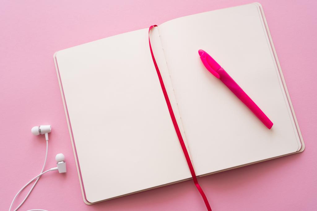 vista superior del cuaderno abierto y la pluma cerca de auriculares con cable en rosa  - Foto, Imagen