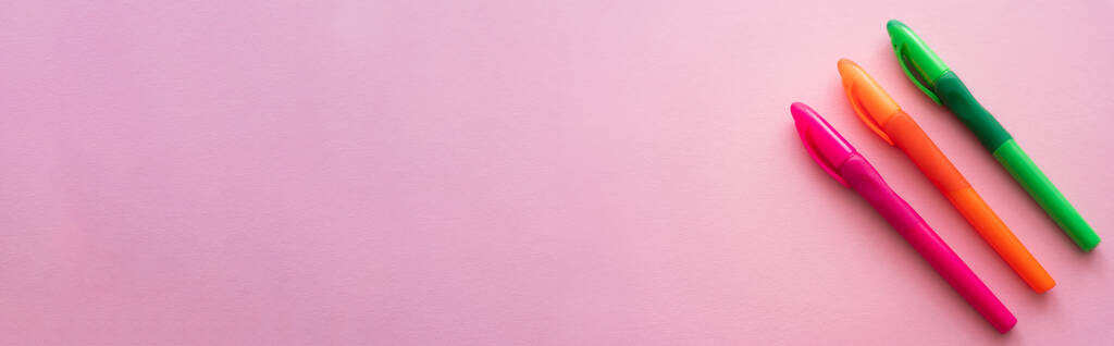 bovenaanzicht van kleurrijke en heldere pennen op roze, banner - Foto, afbeelding