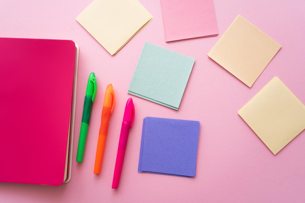 top view of colorful pens near bright notebook and blank paper notes on pink - Photo, Image