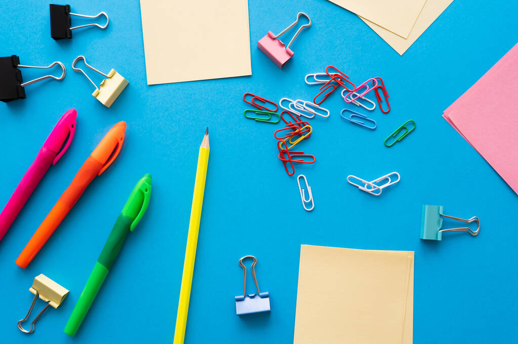 top view of empty paper notes near colorful pens and paper clips on blue - 写真・画像