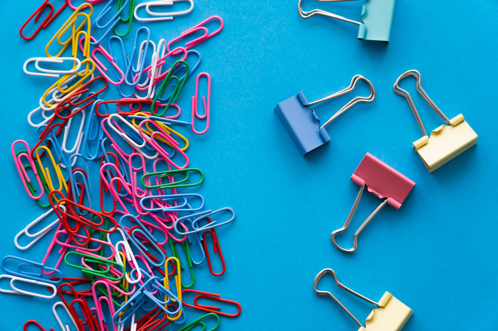 top view of colorful paper clips and fold back clips on blue - Fotó, kép