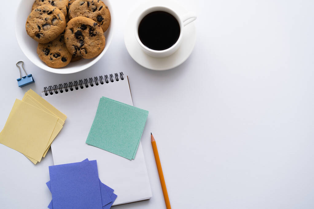 top view of bowl with chocolate chip cookies near cup of coffee and stationery on white - Foto, Imagem