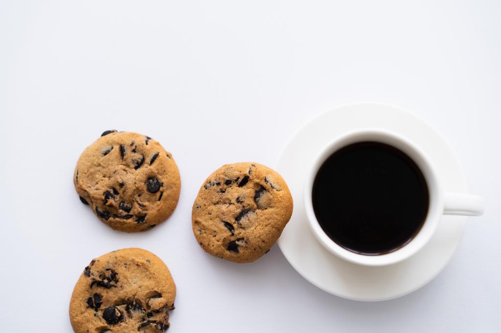 vista dall'alto di tazza di caffè vicino biscotti di gocce di cioccolato su bianco - Foto, immagini