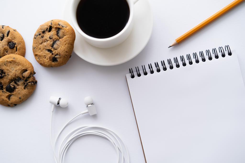 top view of cup of coffee near chocolate chip cookies, stationery and wired earphones on white - Foto, imagen