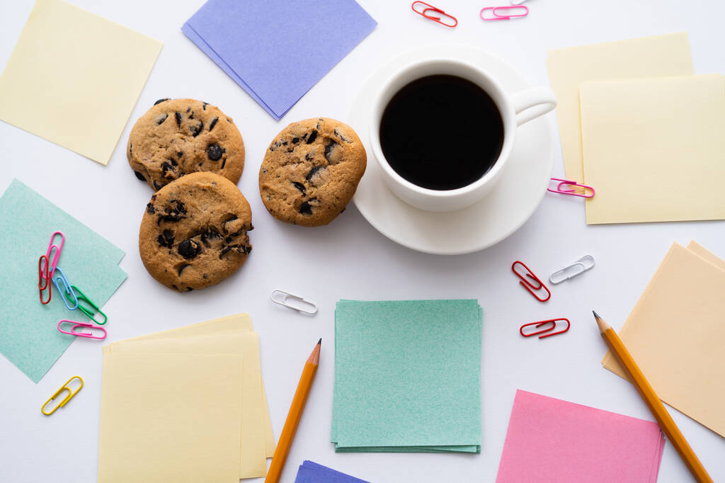 top view of chocolate chip cookies and cup of coffee near stationery on white - Fotografie, Obrázek
