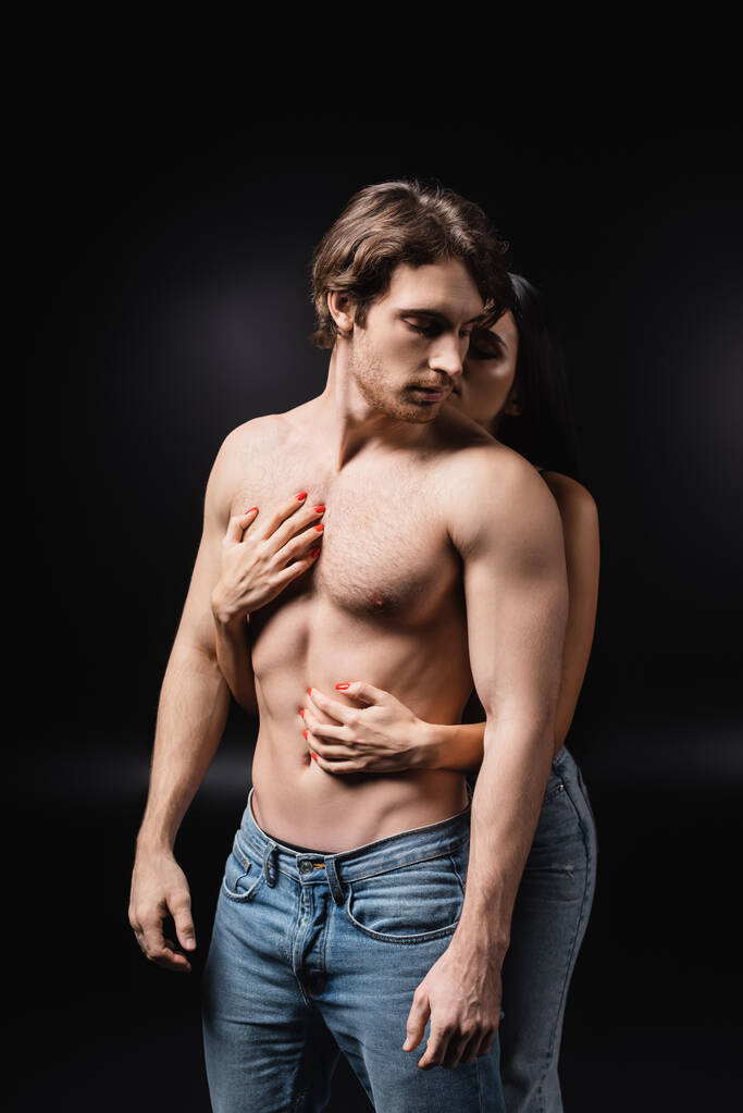 Young woman touching torso of sensual boyfriend on black background - Foto, Imagem