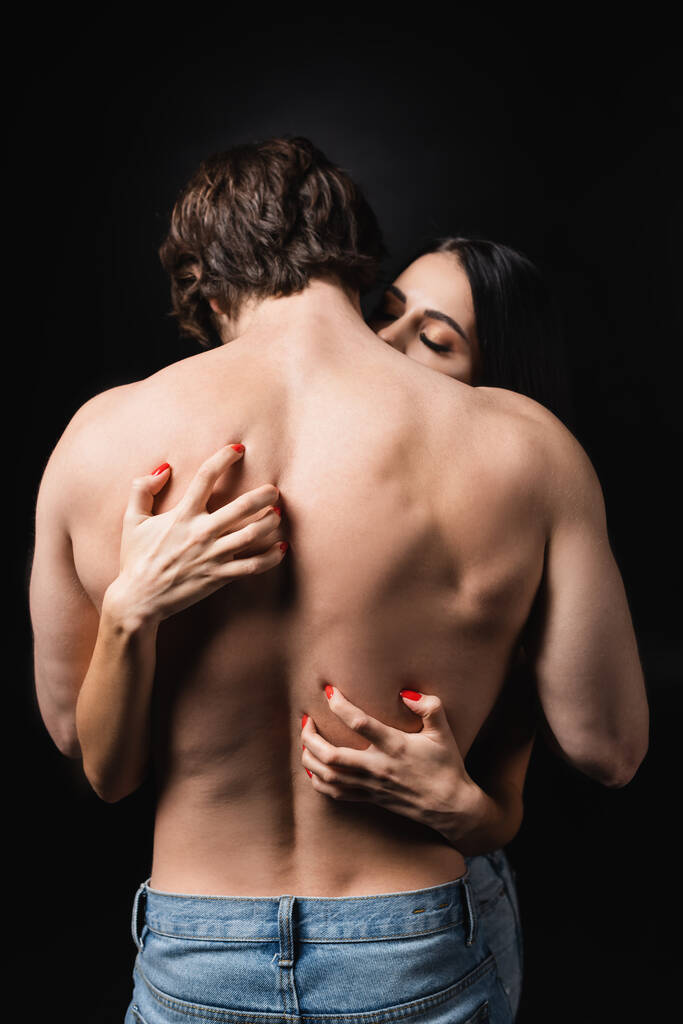 Brunette woman scratching back of shirtless man isolated on black  - Fotó, kép
