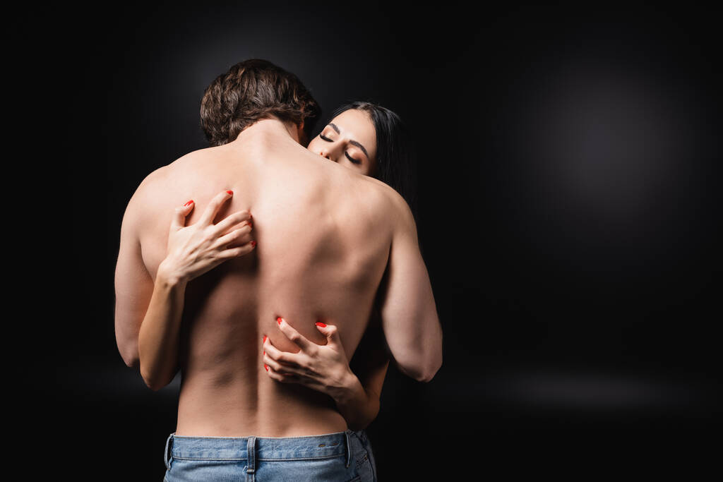 jonge vrouw krassen rug van sensuele vriend op zwarte achtergrond - Foto, afbeelding