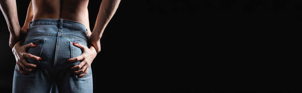 Обрезанный вид женщины, касающейся ягодиц бойфренда в джинсах, изолированных на черном, баннер  - Фото, изображение