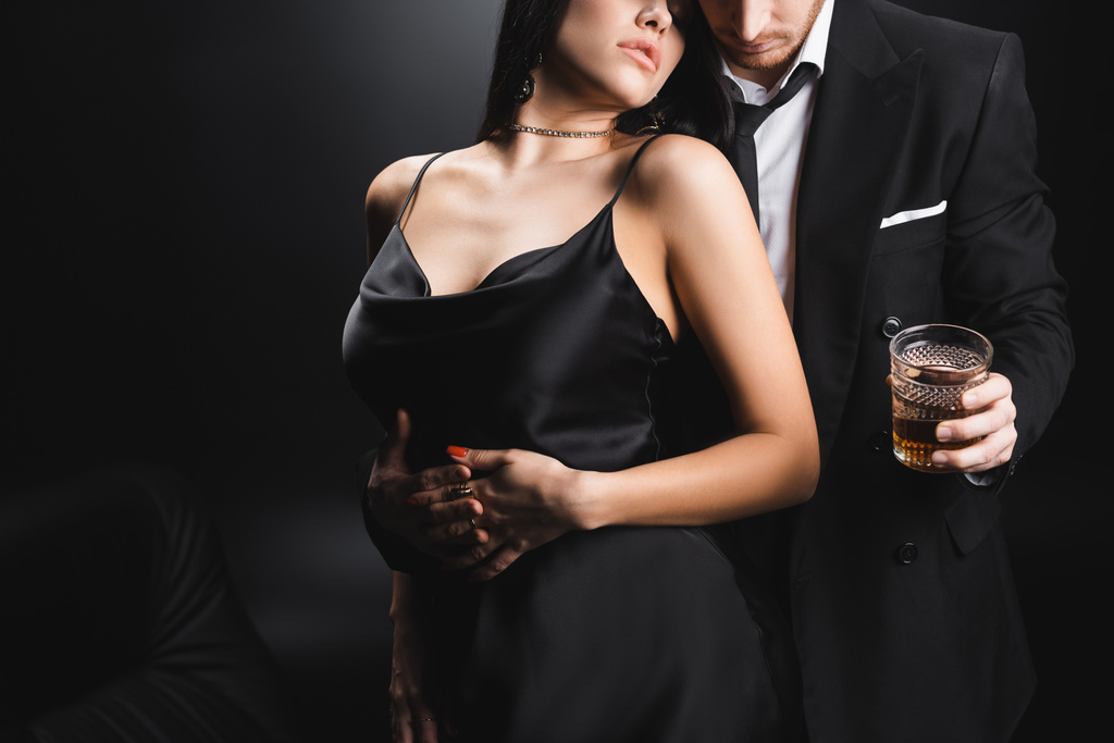 クロップドビューの官能的な女性のドレス立っています近くのボーイフレンドスーツ保持ウィスキー上の黒の背景 - 写真・画像