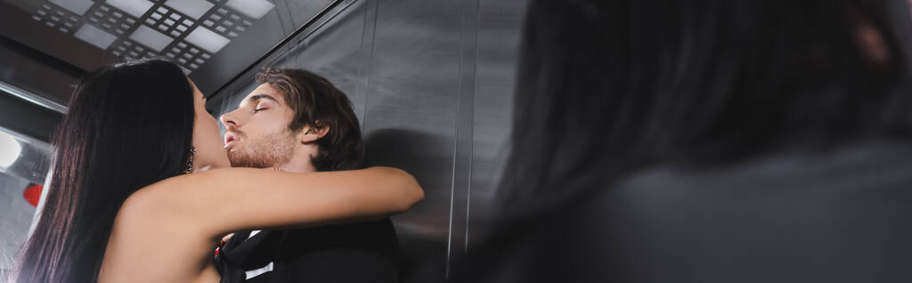 Low angle view of brunette woman kissing elegant boyfriend in elevator, banner  - Fotó, kép
