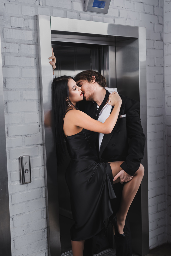 Passionate woman in dress undressing boyfriend near elevator  - Фото, изображение