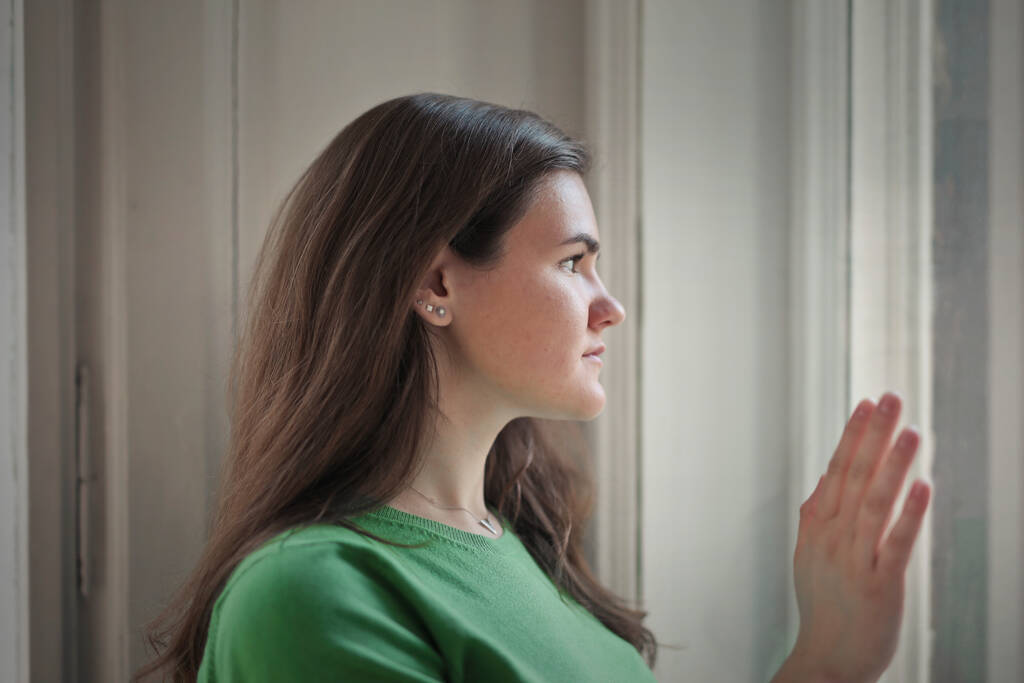 portret van jonge vrouw terwijl kijken uit het raam - Foto, afbeelding