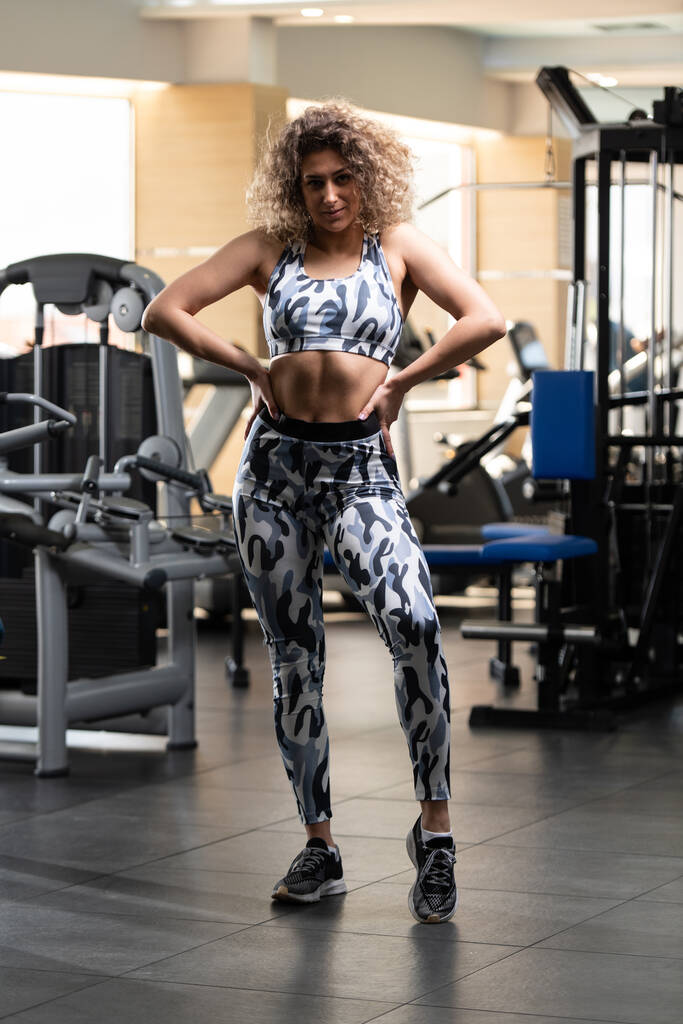 Terve nuori nainen seisoo vahva kuntosalilla ja taivutus lihakset - kaunis urheilullinen kunto malli poseeraus harjoitusten jälkeen
 - Valokuva, kuva