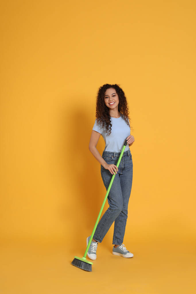 African American woman with green broom on orange background - Photo, Image