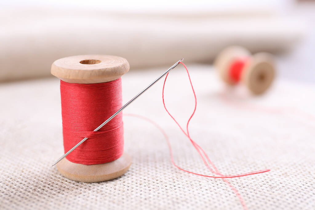 Carrete de hilo de coser rojo con aguja en tela blanca, primer plano - Foto, Imagen