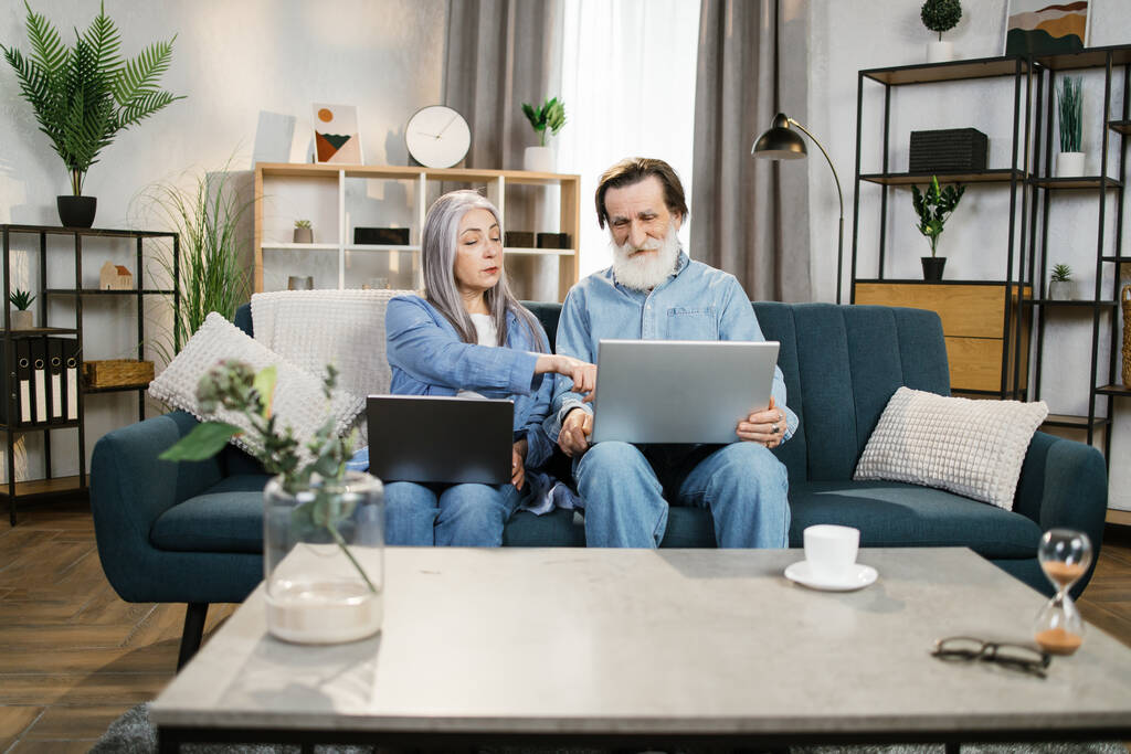 Mature man and woman using laptops, looking at screen. - Photo, image