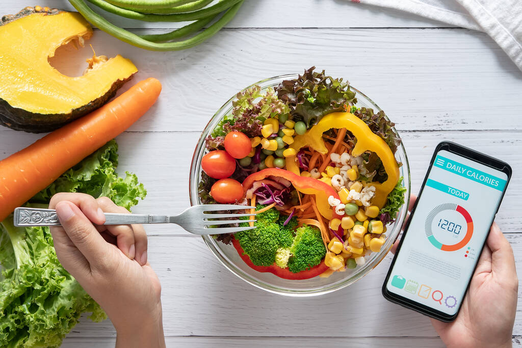 Kalori sayımı, diyet, gıda kontrolü ve kilo kaybı konsepti. Yemek masasındaki akıllı telefon ekranında salata, meyve suyu, ekmek ve taze sebzeyle kalori sayacı uygulaması. sağlıklı beslenme - Fotoğraf, Görsel