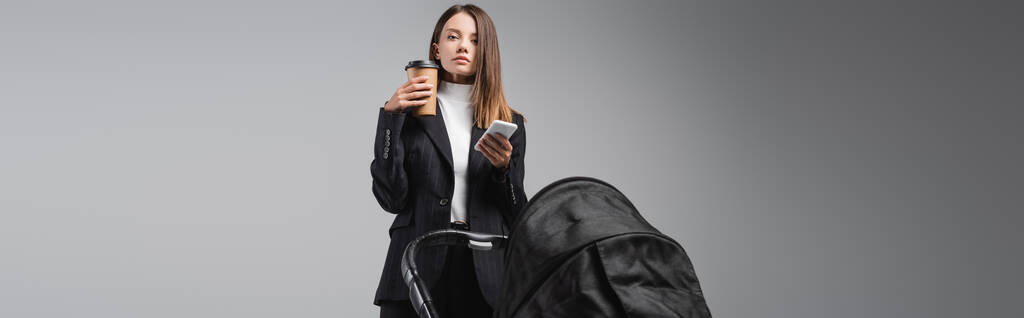 nő okostelefon és kávé menni a kamera közelében babakocsi elszigetelt szürke, banner - Fotó, kép
