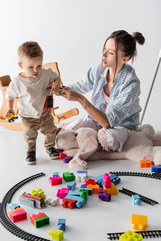 young woman holding toy train while playing with toddler son on white - Zdjęcie, obraz