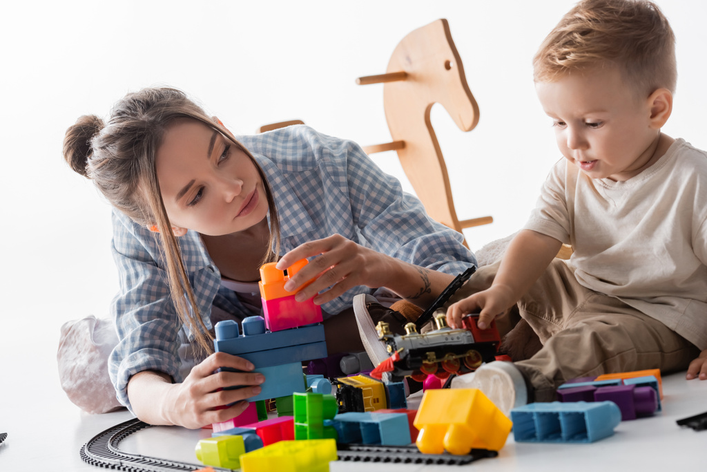 Мать и сын играют со строительными блоками и игрушечным поездом на белом - Фото, изображение