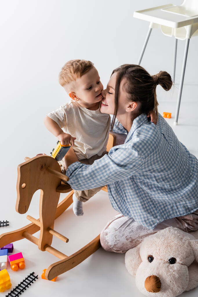 happy woman hugging son sitting on rocking horse on white - Foto, afbeelding