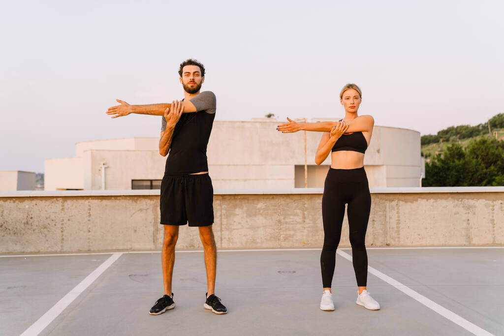 Young man and woman doing exercise while working out together on parking outdoors - Foto, Imagen