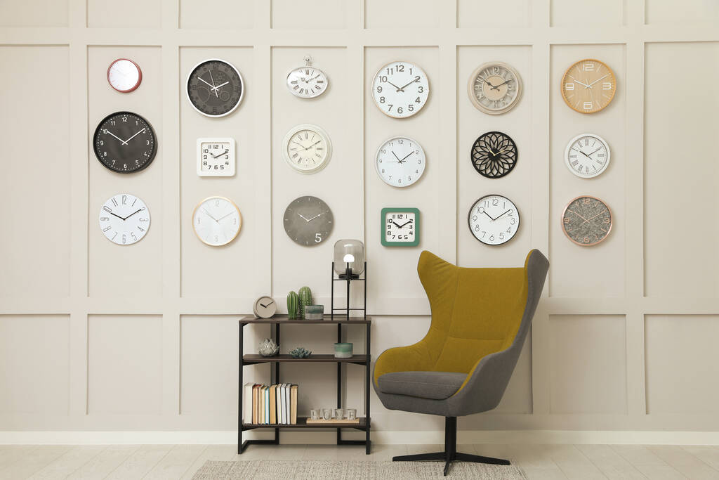 Fauteuil, console tafel en veel verschillende klokken opknoping op witte muur in de kamer - Foto, afbeelding