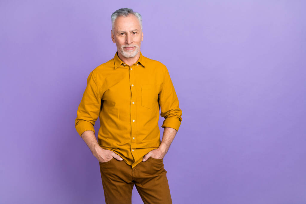 クールな長老グレーの髪の男の写真紫色の背景に隔離された黄色のシャツを身に着けている - 写真・画像