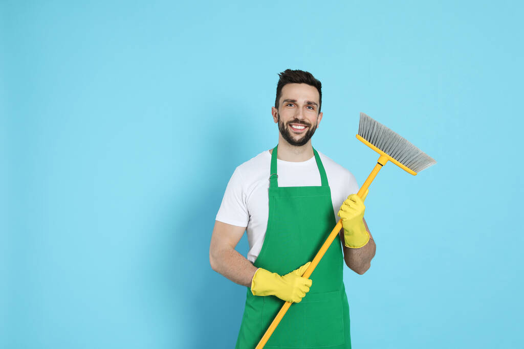 Man with yellow broom on light blue background, space for text - 写真・画像